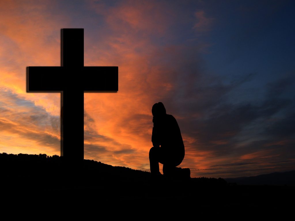 Is Confession Good for the Soul? A person kneeling in front of a cross, silhouetted by a sunset