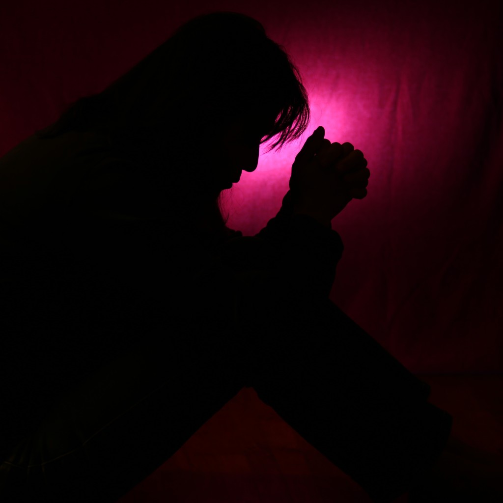 Will God Listen to Your Prayer? Person sitting in the dark, hands folded, saying a prayer.