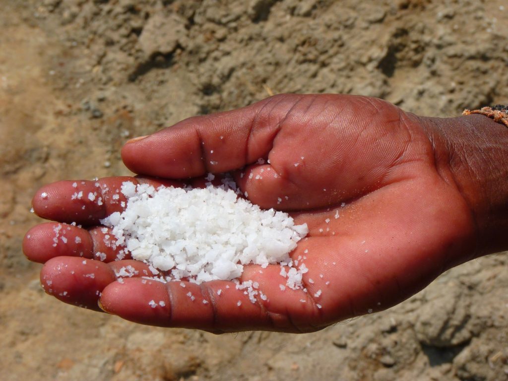 Obedience or Rebellion_open hand holding coarse salt, some salt spilling out onto sand below