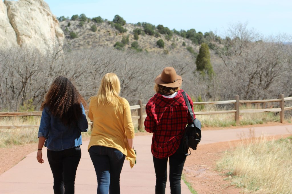 Who Will You Walk With_three female friends walking on a path with scrub grass shrubbery on a hill in the background