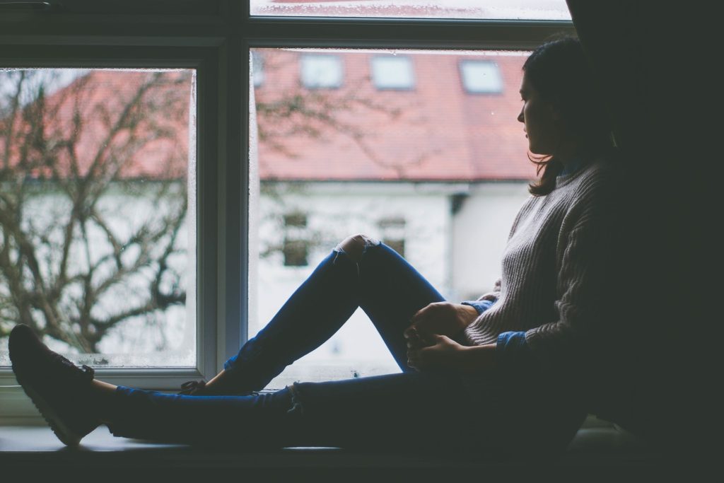 How to Handle Your Burdens_young woman sitting on window sill, looking out window to gray day