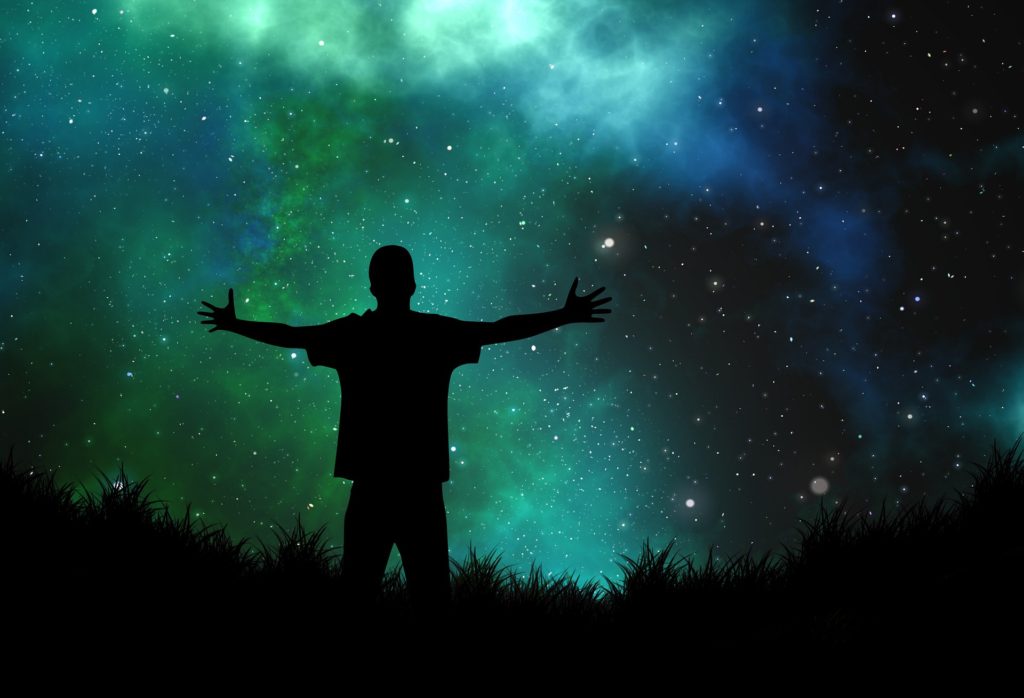 Give Thanks and Watch It Change Your Life_man standing with outstretched arms, silhouetted against a blue-green night sky filled with stars