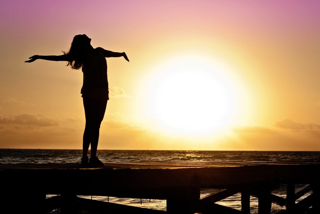 When You See the Deliverance of the Lord_woman standing on boardwalk over water, arms outstretched, chin toward sky, silhouetted against the sunset