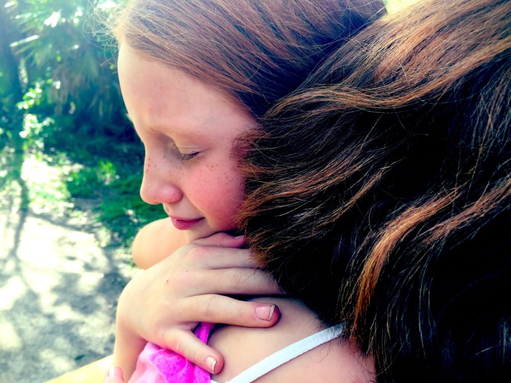 Young girl, eyes closed, hugging a girl or woman