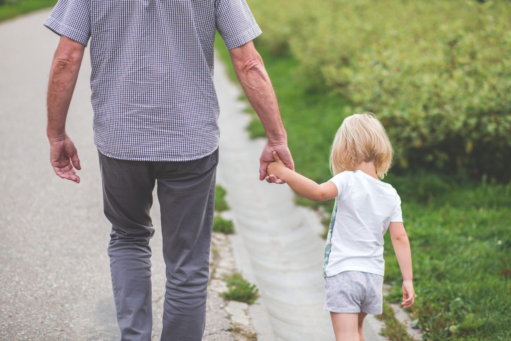 A view from the rear of a little girl holding her father's hand, walking on the side of a road