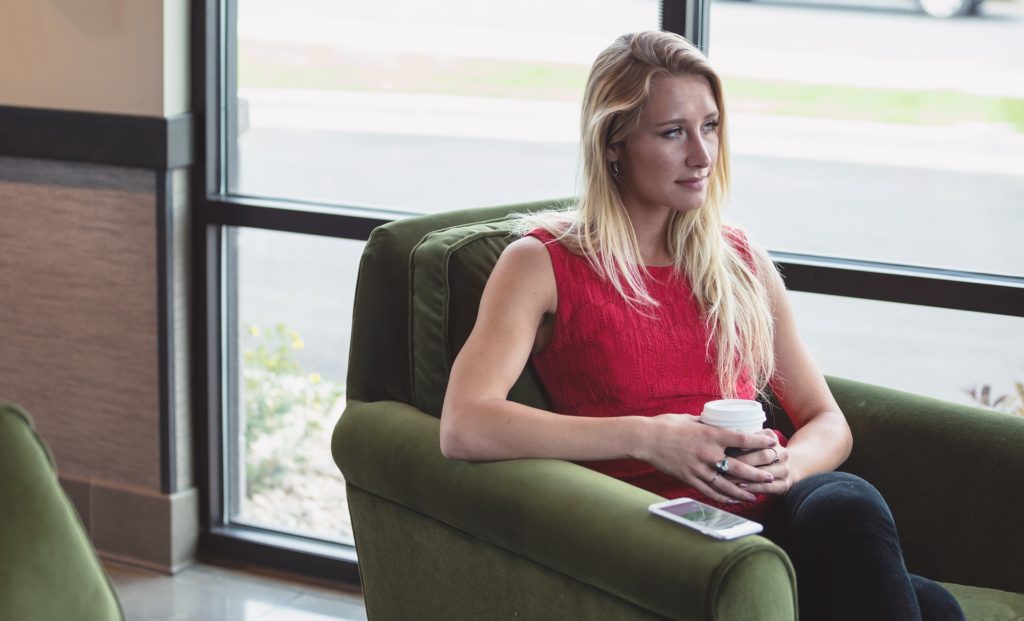 You prayed and bargained and pleaded, but the person wasn't healed, the heart was not changed. What does it mean when you don't get the miracle you wanted? Woman in red tank top looking bummed, sitting, holding coffee, phone on arm of chair