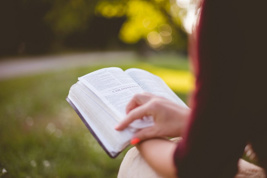 Woman reading an open Bible, green landscape in background